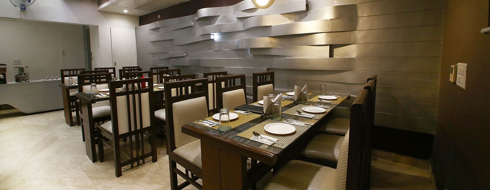 Uniformly placed chairs and tables of mocha and dark shades  in a modern light setting an extremely detailed walls and interior - Hotel Emerald, Chandigarh