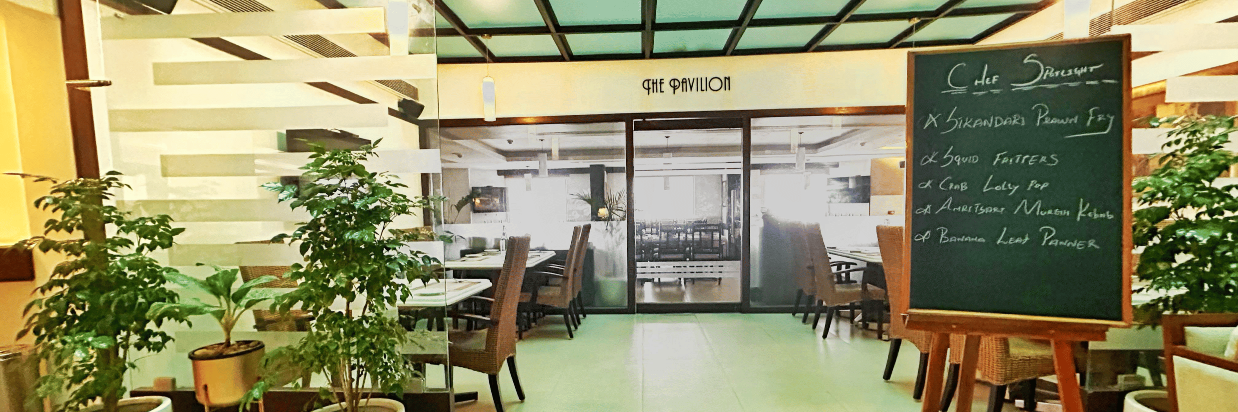 Entrance to the hotel restaurant featuring modern interiors, indoor plants, and seating arrangements.