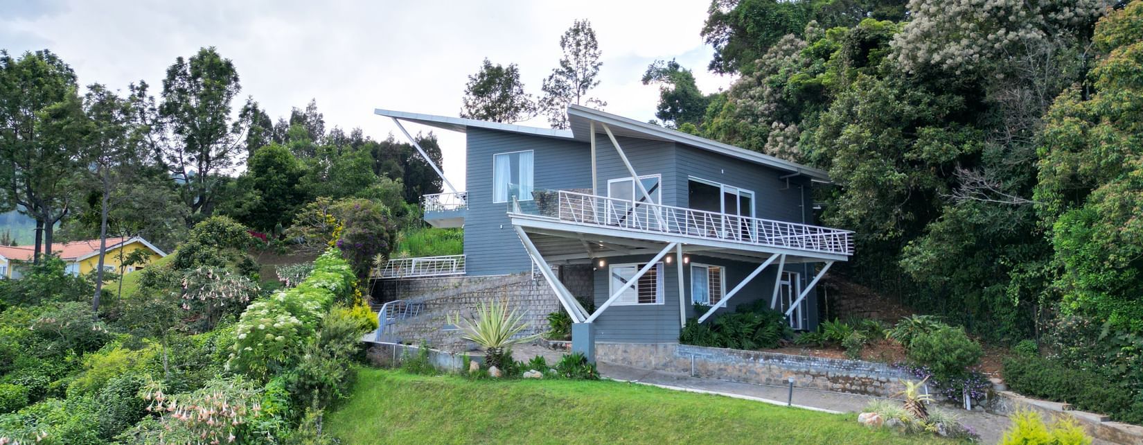 Front view of a contemporary house situated on a grassy hill with trees in the background at Ibex Resorts, Coonoor (Tapas).