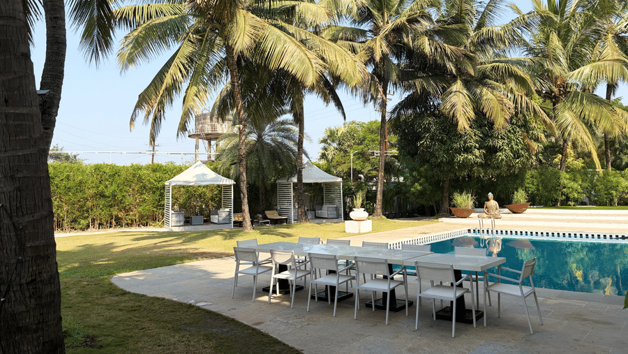 The Mansion House resort poolside dining with long white table, chairs, canopy tents, palm trees, and tall structure, offering a tropical and inviting atmosphere for gatherings.