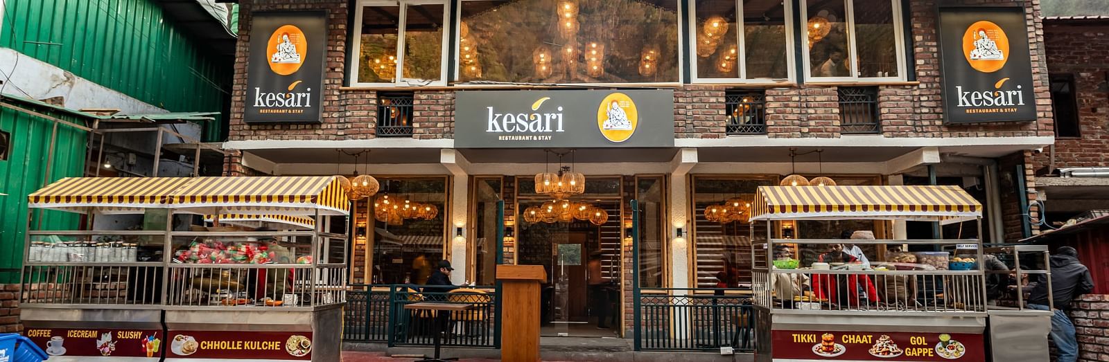 Facade of the Kesari Restaurant with two stalls selling various Indian fast foods with a clear blue sky in the background.