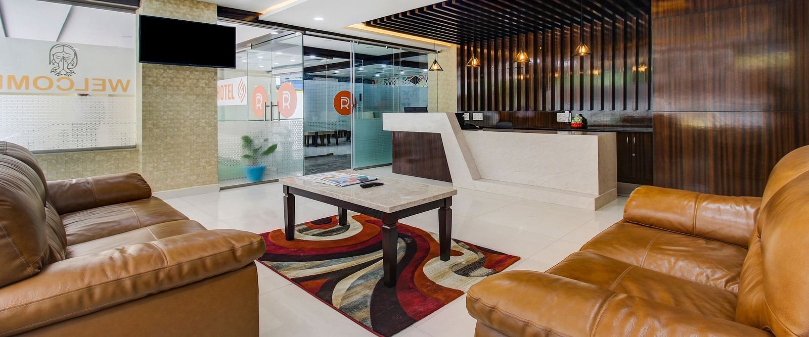 A lounge corner with a comfortable brown leather sofa set, a patterned rug, and a glass partition with hotel branding.