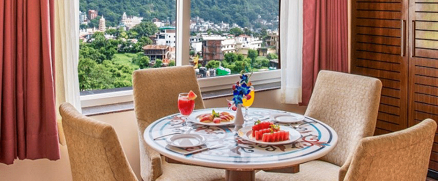 A dining table surrounded with four cushioned chairs overlooking beautiful mountain views from the window of the suite at Regenta Inn DLS.