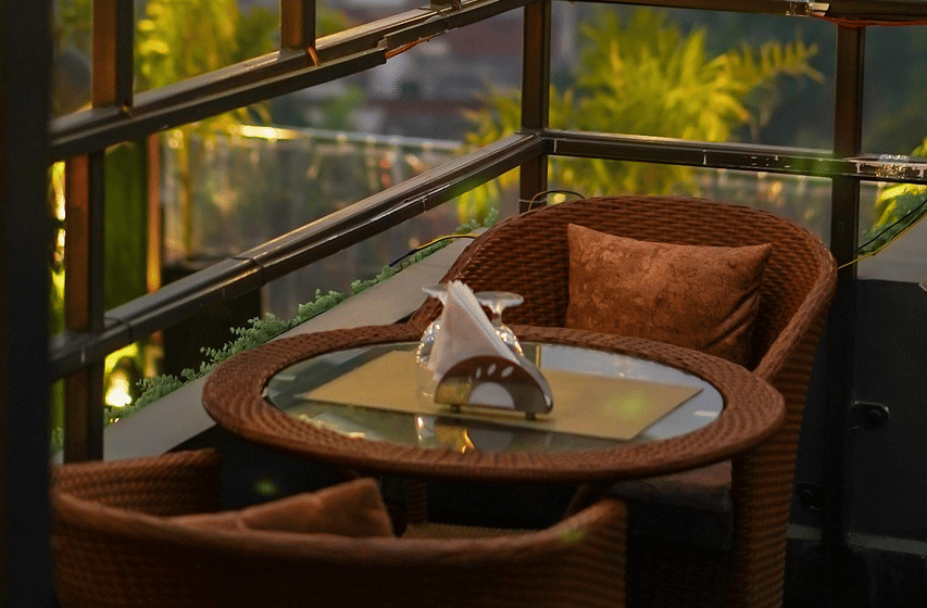 Two chairs facing each other on a terrace with warm lights besides it on a late evening.