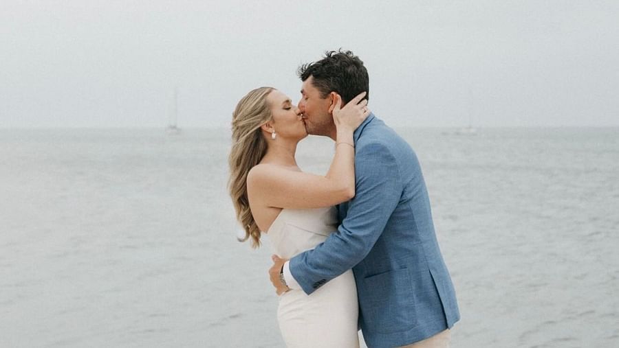Bride and groom kissing each other in front of the ocean with a soft, cloudy sky as the backdrop.
