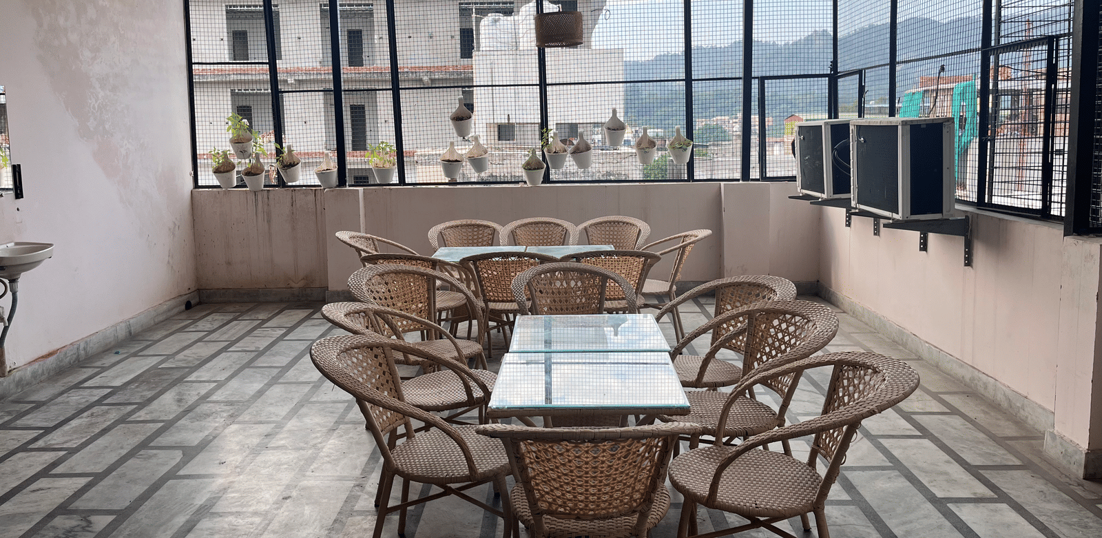 2 dining tables featuring a glass surface lined with bamboo chairs on the rooftop dining area at Perfectstayz Value Dhruv Nanda, Haridwar.