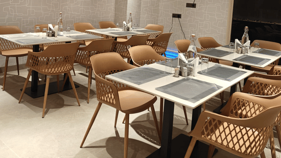 Modern indoor dining area at Hotel Bluestone Prime featuring neatly arranged tables with place settings, cushioned chairs, warm ambient lighting, and a clean contemporary design. The spacious layout offers a comfortable atmosphere suitable for relaxed meal