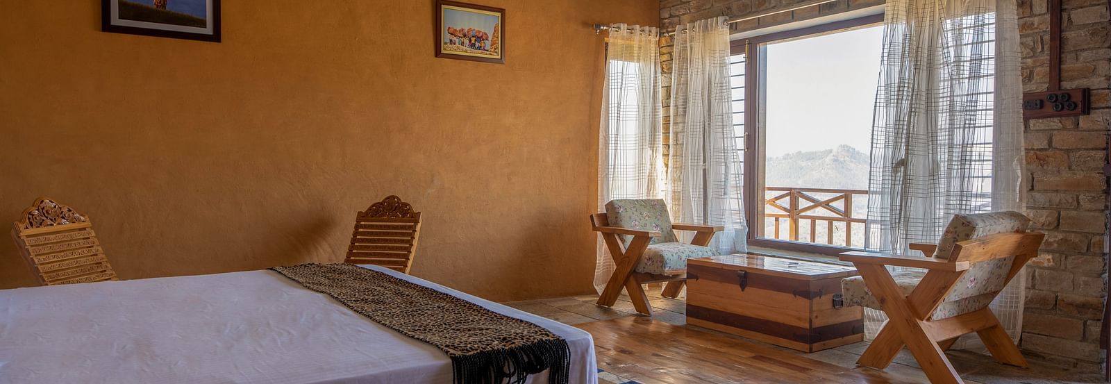 Rustic room with a bed, wooden chairs, stone wall, and a window with a mountain view. - Blusalzz Homes The Himalayan Bungalow, Almora