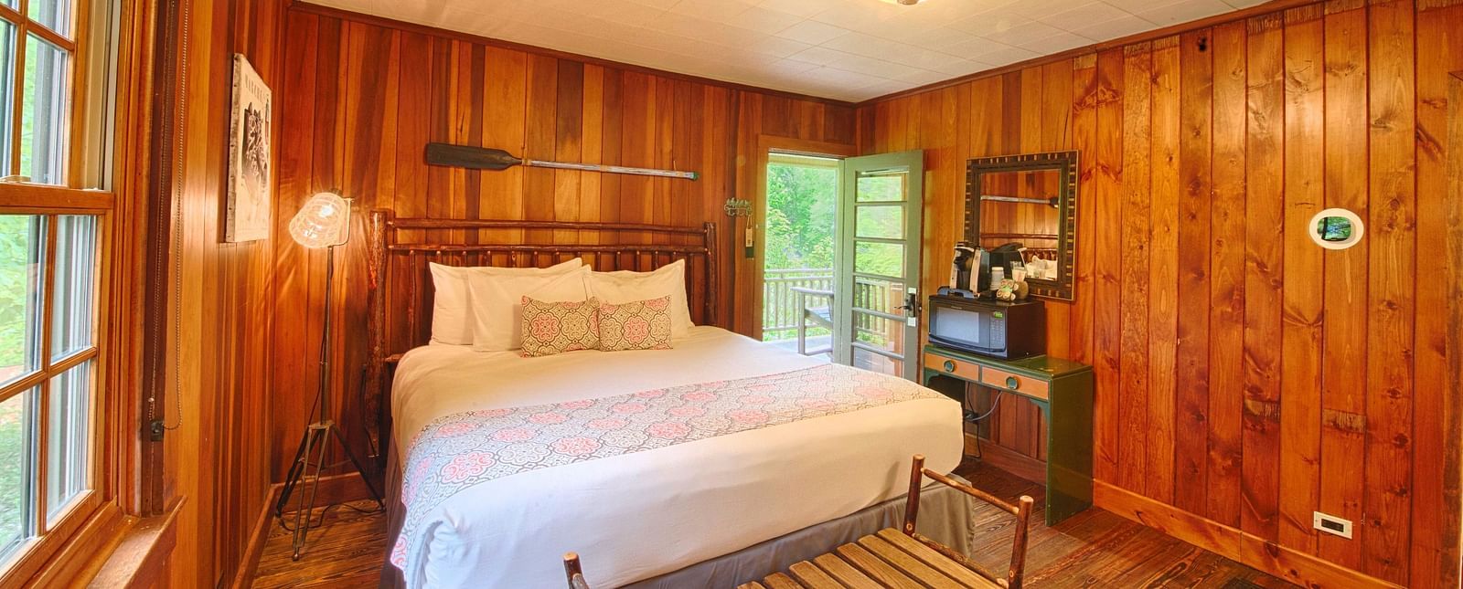 front view image of a cozy double bed in a room with wooden walls and flooring with a small chandelier - Historic Tapoco Lodge