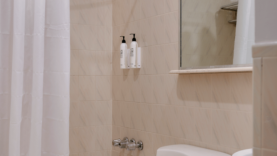 Bathroom at Night Hotel Broadway with bathtub, shower curtain, toilet, sink, and wall mirror.