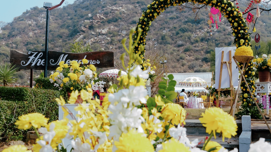 An outdoor scene at Valley By Grassfield, with a large flower vase, a decorative archway, and a hill in the background.