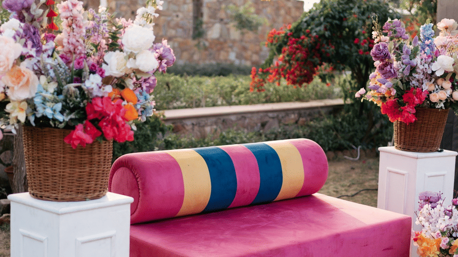 An outdoor event space at Valley By Grassfield, under trees with a couch, colorful cushions, and floral decorations.
