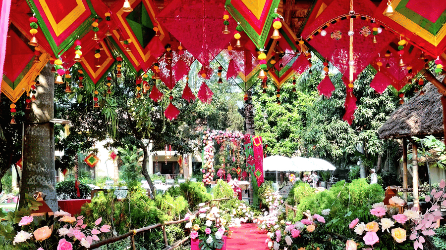 A vibrant wedding venue setup at Vedic Village Spa Resort featuring colorful kite shaped decorations pink and green floral arrangements and a decorated red carpet pathway in an outdoor setting.