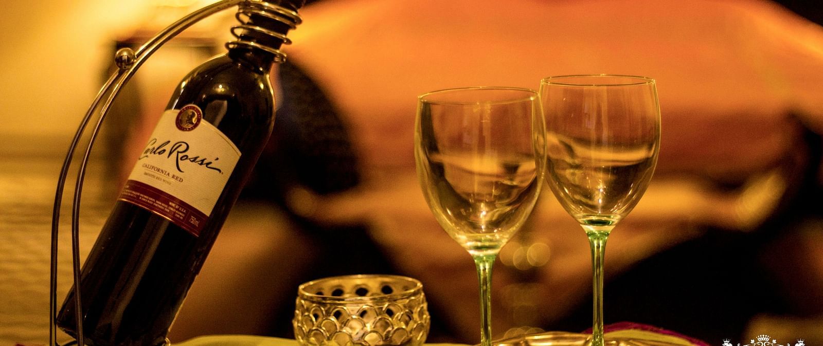A bottle of wine and two glasses set on a table at Umaid Vilas Jaipur, with a blurred background suggesting a room setting.