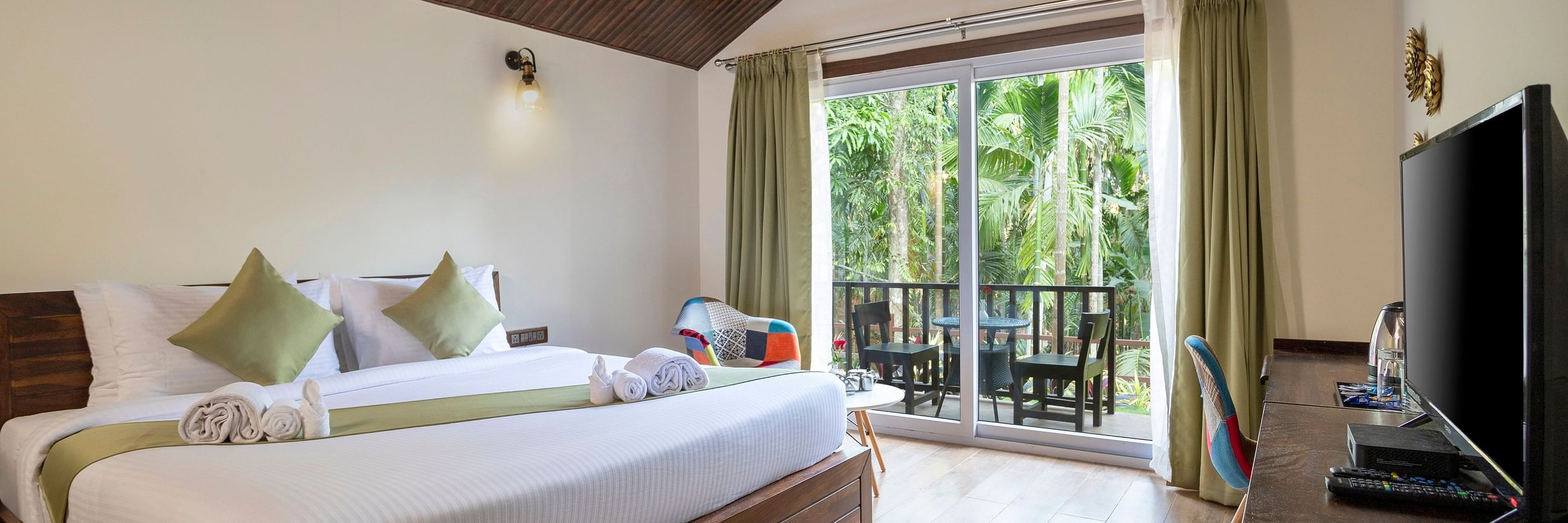 A hotel room with a garden view, a wall mounted television and a large bed - Stone Wood Nature Resort, Gokarna