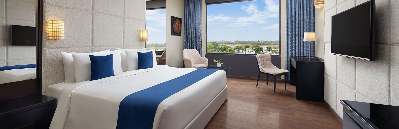 Image of a room with bed, seating area and large windows on the side at Essentia Luxury Hotel, Indore