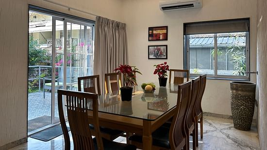 A sophisticated dining area with a polished wooden table, elegant chairs, and large glass windows – Maxxvalue Klub Klass Villa, Lonavala.