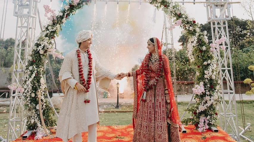 A bride and groom exchanging vows under a floral archway, with colorful drapes in the background.