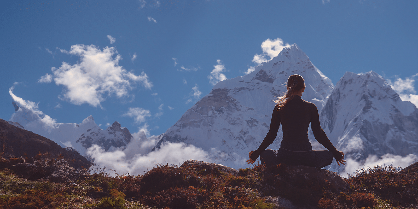 a woman meditating cross legged on a mountaintop