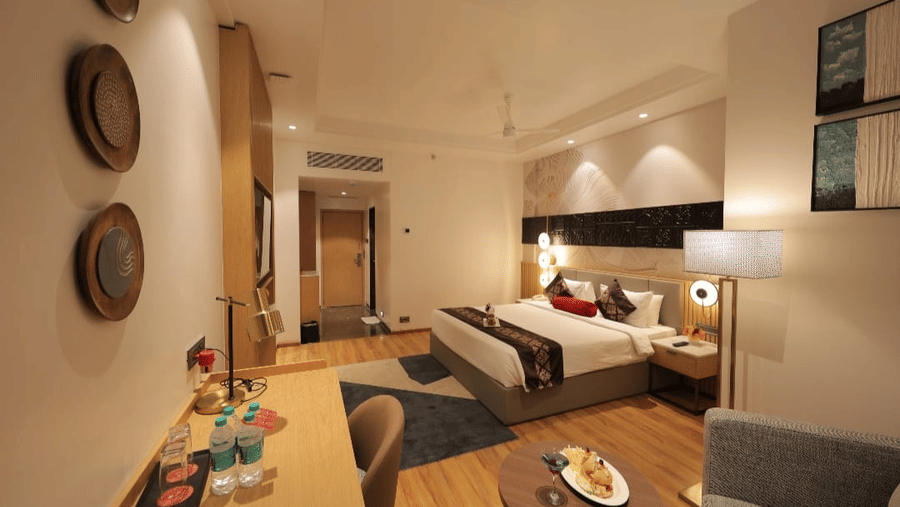Well-appointed guest room at Lords Inn Somnath with a comfortable bed, elegant wooden interiors, bedside lighting, seating area and contemporary decor.
