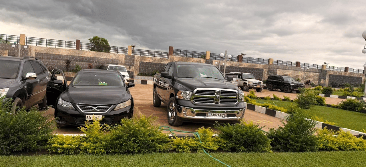 A wide shot of a modern building's exterior with two parked black SUVs, a lawn area, and a cloudy sky at Luffu Club.