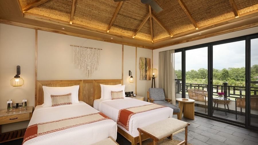 Room with twin beds, fan, TV, and scenic outdoor view from balcony - Royal Tulip, Chitwan