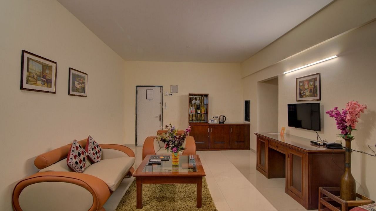 a living room with a sofa facing a mounted television - Camel Valley Resort, Igatpuri