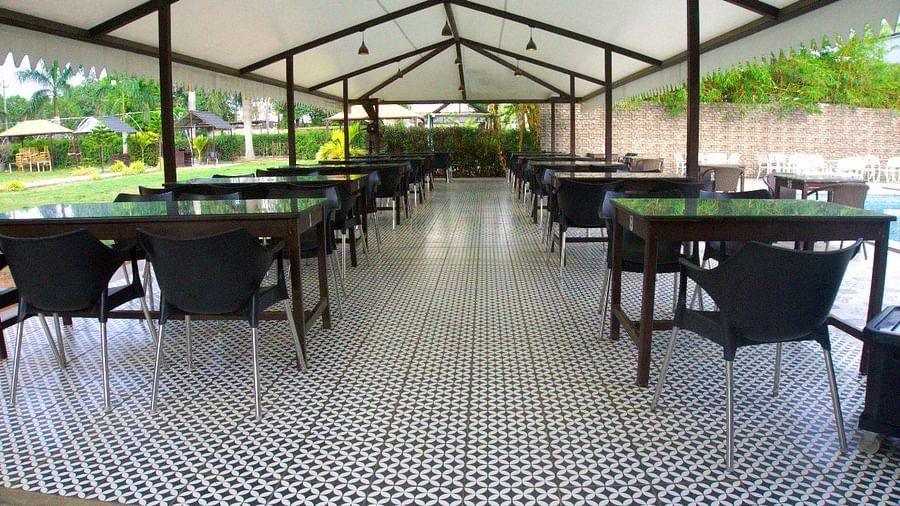 Covered outdoor dining area next to a pool and lush garden. | Vistar Resort, Bengaluru