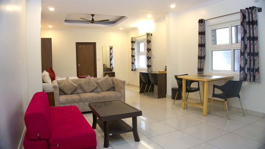 A beige sofa, red armchair, glass coffee table, and a plush bed in the background. | Vistar Resort, Bengaluru