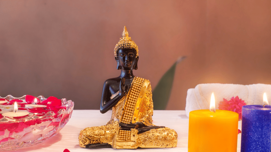 A statuette of lord Bhudda placed on a table with lit candles and rose petals at Lords Inn Jamnagar