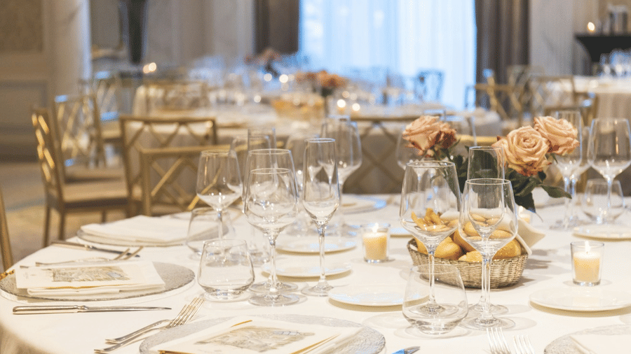 a close-up shot of a round table with white ceramics, silver cutlery set, and a floral decoration at the centre