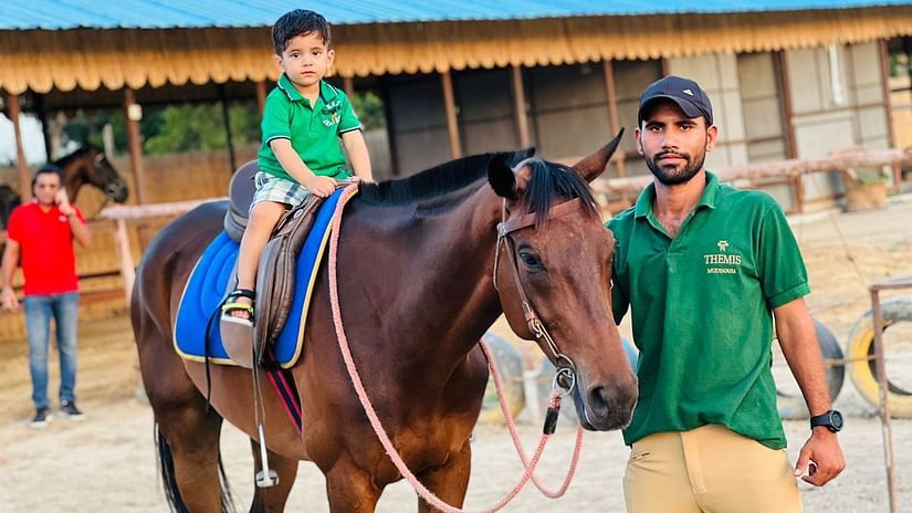  a man helping a kid in horse riding at Themis Mudhouse - A Nature's Retreat Resort & Wellness