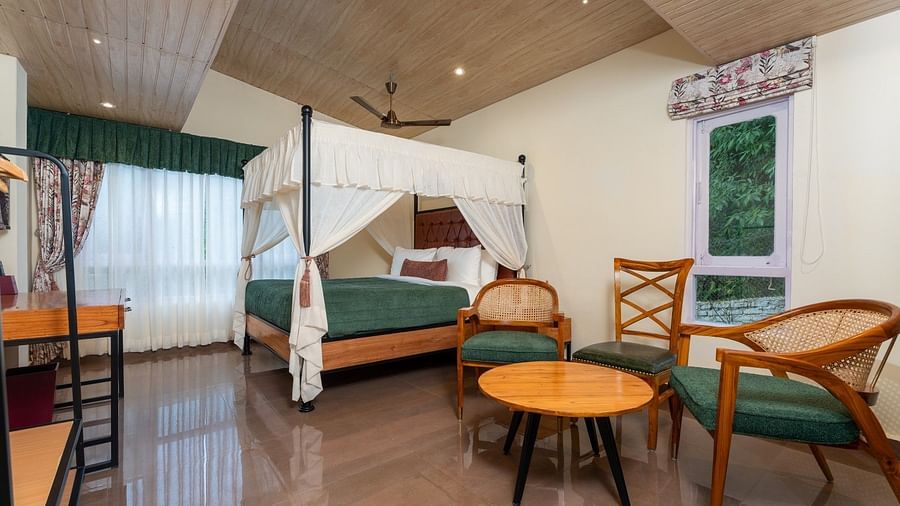 Premium Room featuring a large bed with curtains neatly tied to rods on all four sides, also includes chairs and tables arranged neatly.