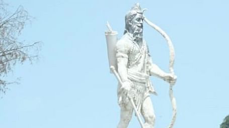 A white statue of Lord Parshuram standing on a podium with a sea on the background.