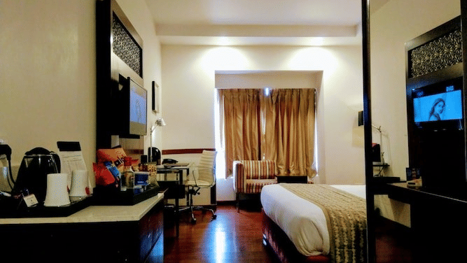 A room with double bed, TV, coffee station, windows with curtains and wooden flooring