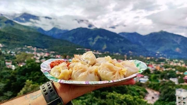 A man holding a plate of momo with hills on the background.
