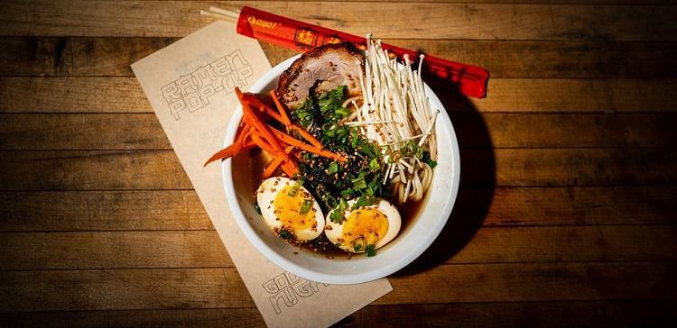 Overhead shot of a bowl with food and chopsticks on a wooden table. 