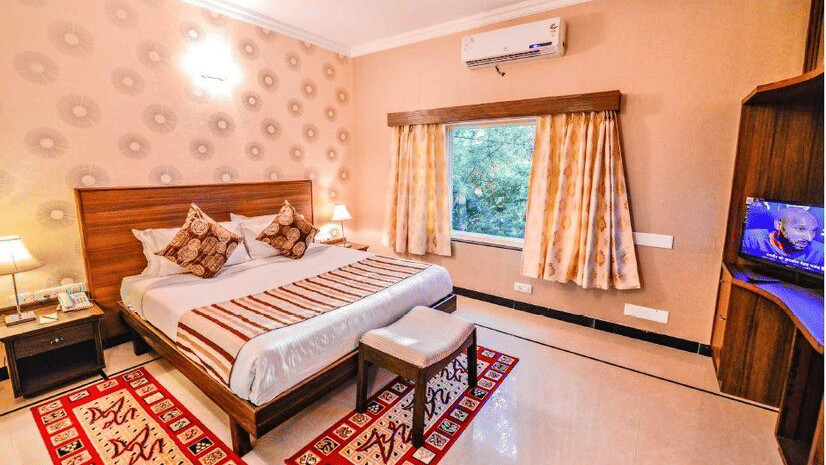A bedroom featuring twin beds, patterned wallpaper, a red floor runner, wardrobe, and a wall-mounted television at Amantra Shilpi Resort, Udaipur.