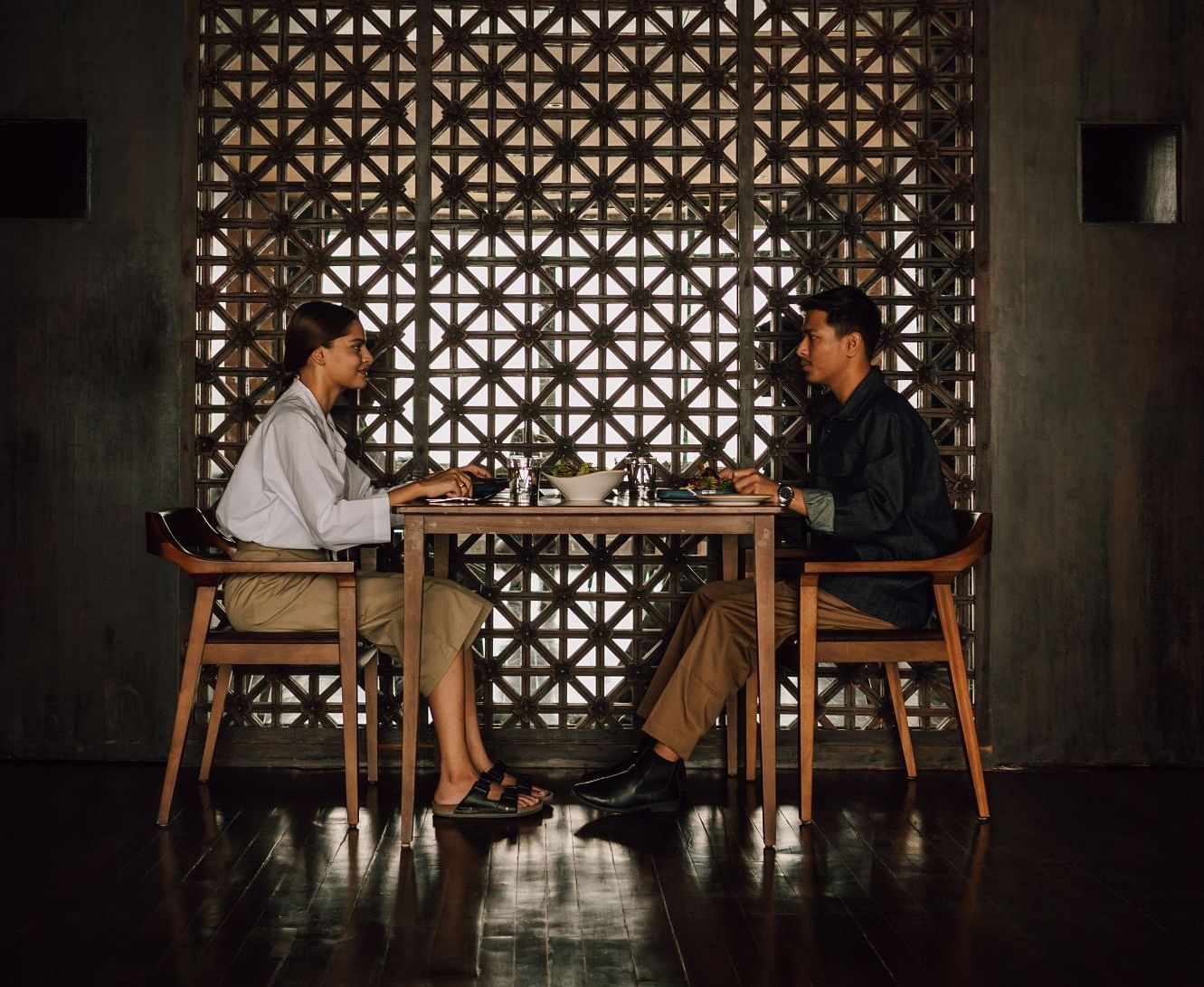 Two people dining in a restaurant with a lattice-patterned wall, creating an intimate and elegant ambiance.