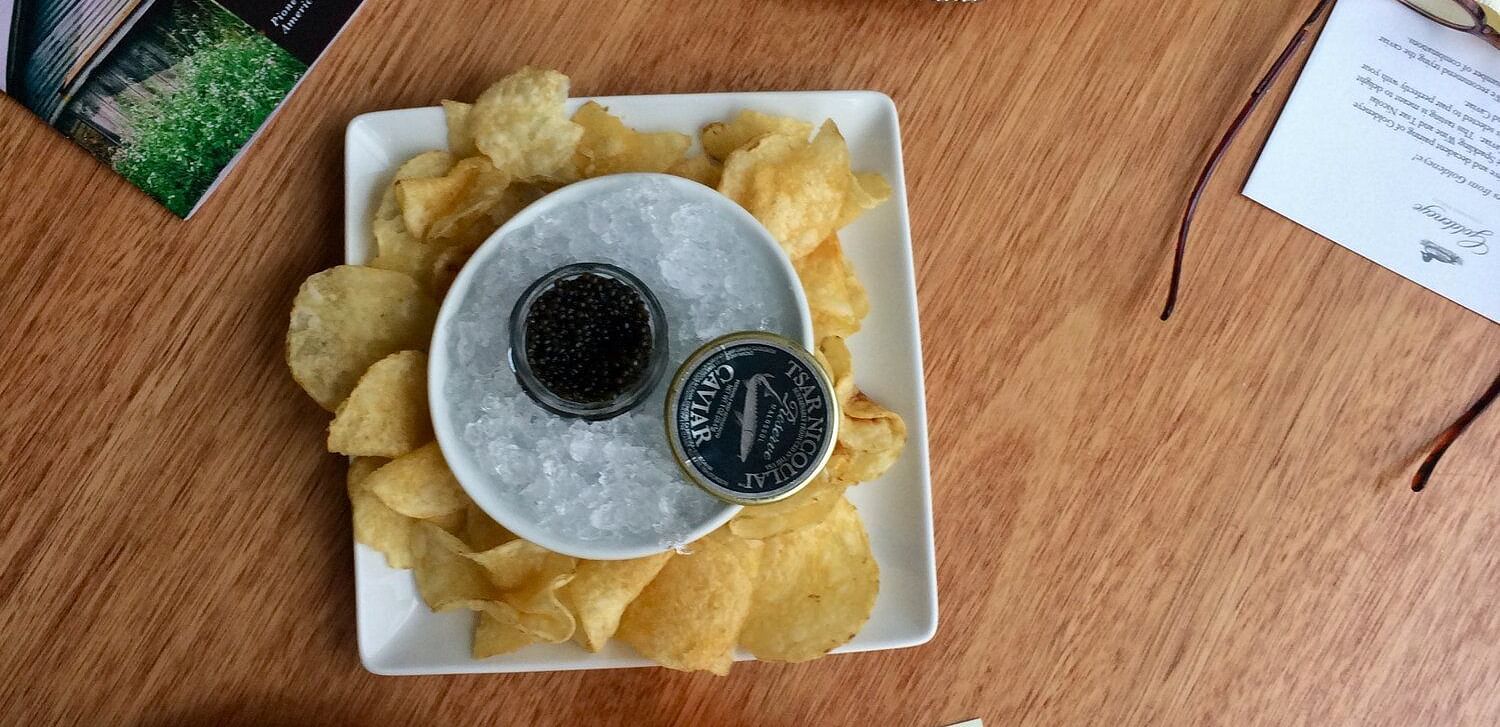 An image of a dinner table where several plates are placed with food items on it like chips, scarmbled eggs, leafy vegetables, cream, and some tapioca seeds