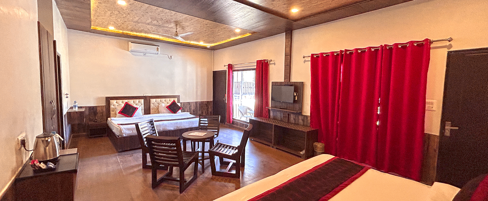 A Family Cottage with beds facing towards each other seperated by a round dining table and TV at DLS MJ River Resort, Rishikesh.
