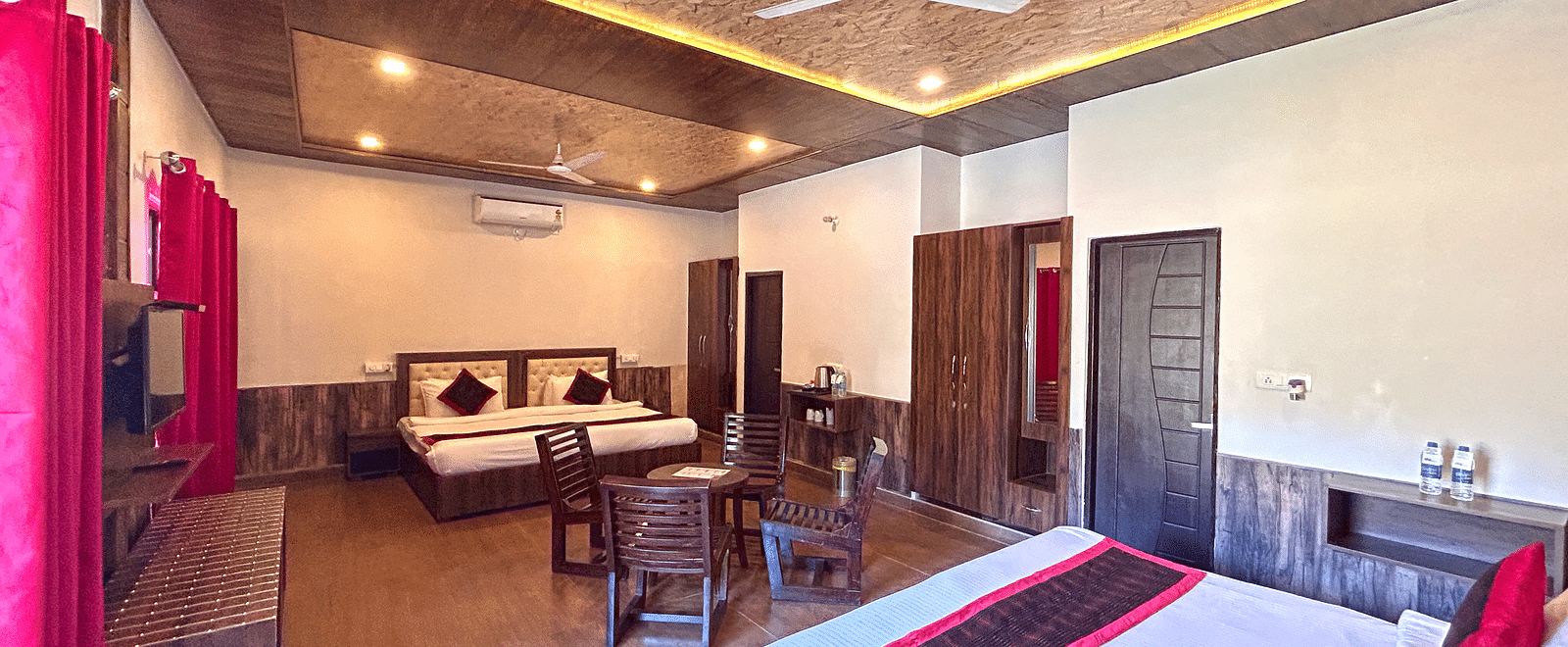 A Family Cottage with beds facing towards each other seperated by a round dining table and TV at DLS MJ River Resort, Rishikesh.