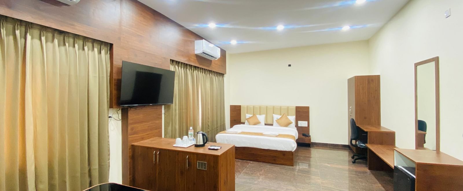  A wide shot of a hotel room at Hotel Sahara Tree, showing a television, bed, wooden furniture, and a dressing area.