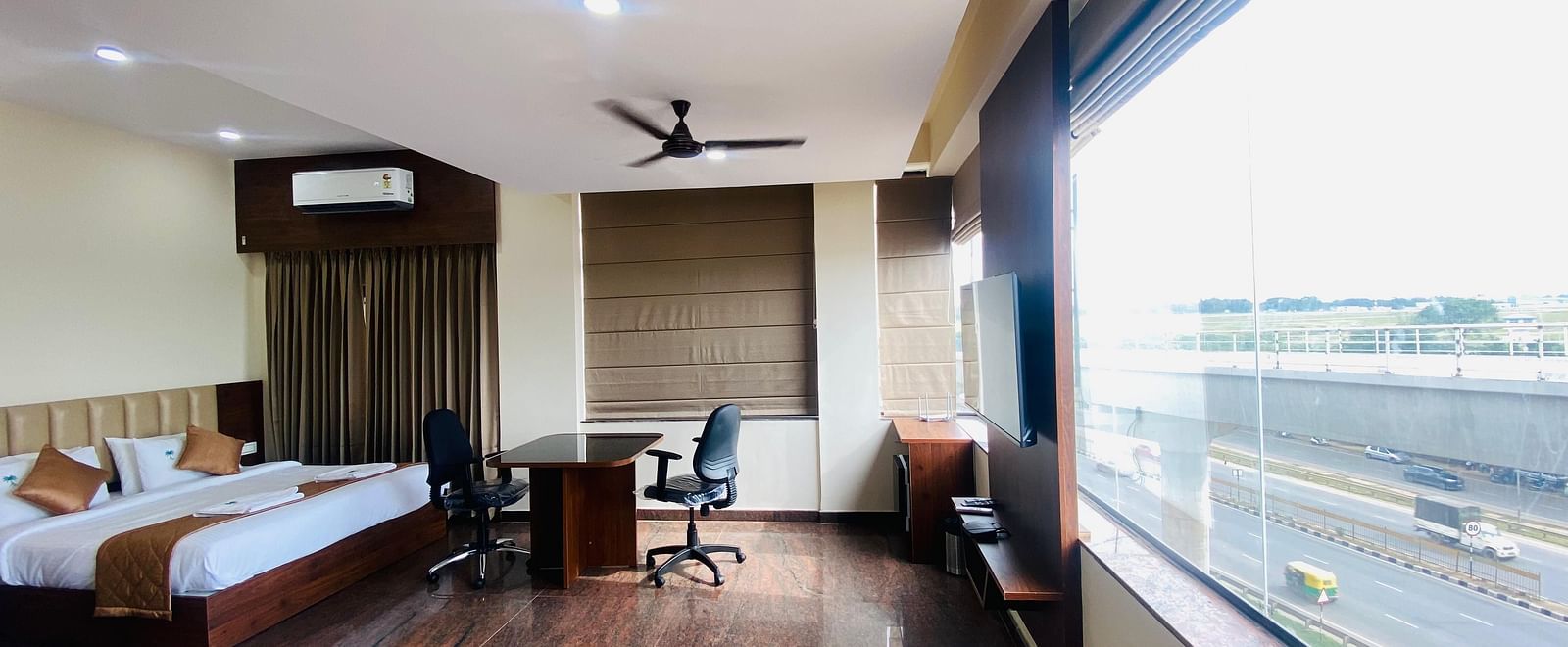 A bright room at Hotel Sahara Tree with a large window view, bed, and desk.