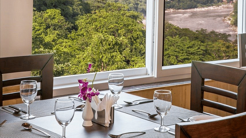 A close up shot of a dining table with table mats and glassware with a huge window behind it at Regenta Inn DLS.