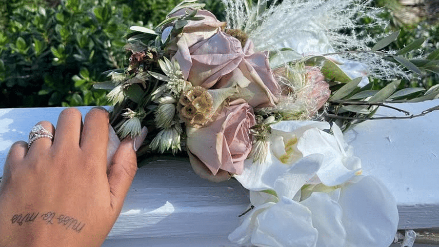 A hand holding a wedding bouquet of roses and orchids with ocean and trees in the background | A Stone's Throw Away 