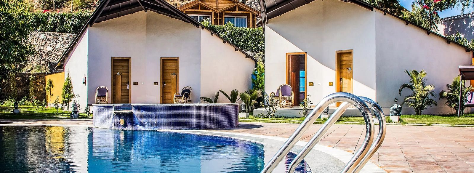 Two modern bungalows with pointed roofs flank a swimming pool.