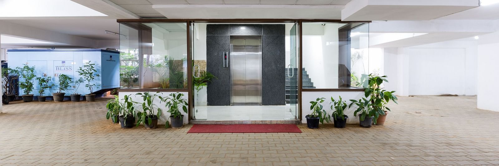 An entrance to a building with potted plants on either sides and an elevator and generator in the background - Sanctum Suites BEL Road, Bangalore