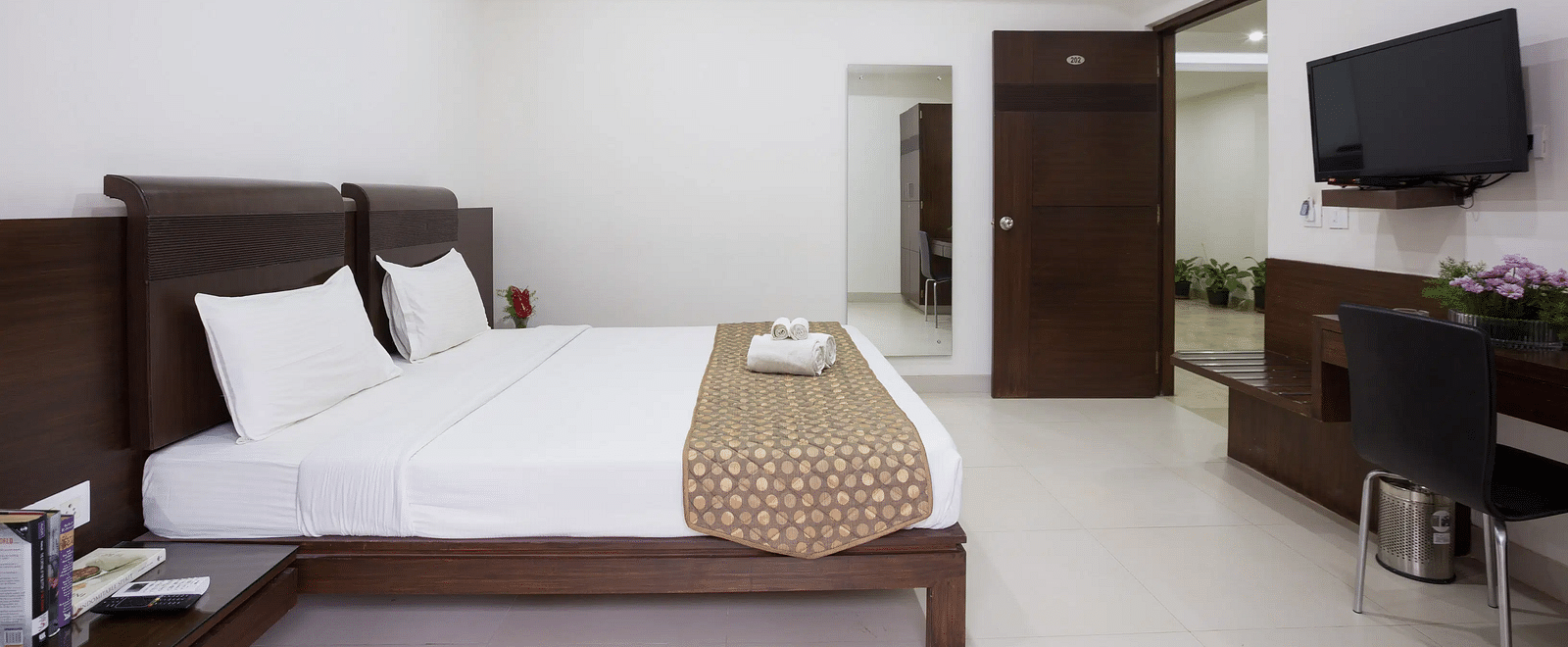 A bright hotel bedroom with a double bed, white linen, a television, and air-conditioning - Sanctum Suites BEL Road, Bangalore