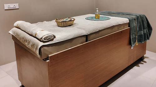 A spa room at ABN Sarovar Portico, Jim Corbett featuring a air-conditioner, a comfortable, high-raise bed which has a pillow, a basket with spa products, and a bottle of massage oil on it.
